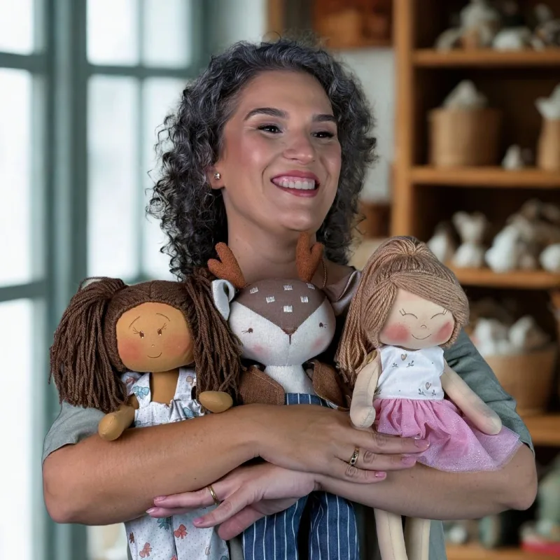 Eu sorrindo segurando três bonecas de pano feitas à mão